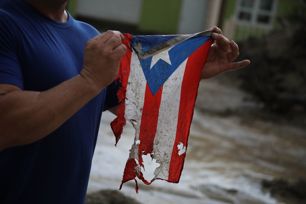 Photograph of resident holding torn flag of Puerto Rico damaged by Hurricane Maria